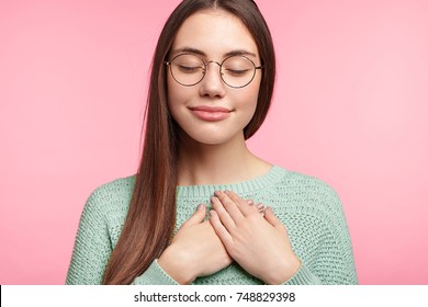 Faithful woman closes eyes and keeps hands on chest near heart, shows her kindness or favour, expresses sincere emotions, being kind hearted and honest. Body language and real feelings concept