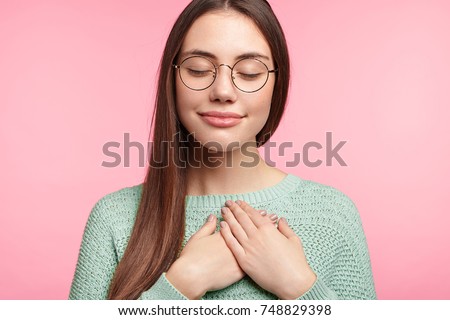 Faithful woman closes eyes and keeps hands on chest near heart, shows her kindness or favour, expresses sincere emotions, being kind hearted and honest. Body language and real feelings concept