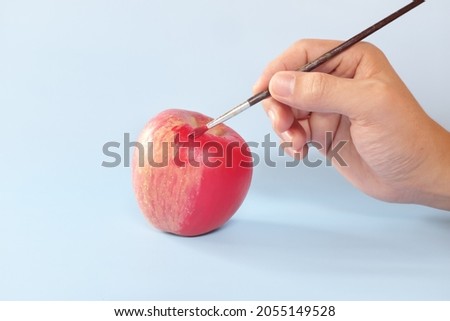 Fake food, coloring, fraud and fraudulent food concept. Hand painting an apple with artificial red colorant or paint.