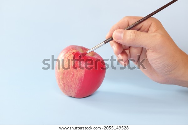 Fake food,\
coloring, fraud and fraudulent food concept. Hand painting an apple\
with artificial red colorant or\
paint.
