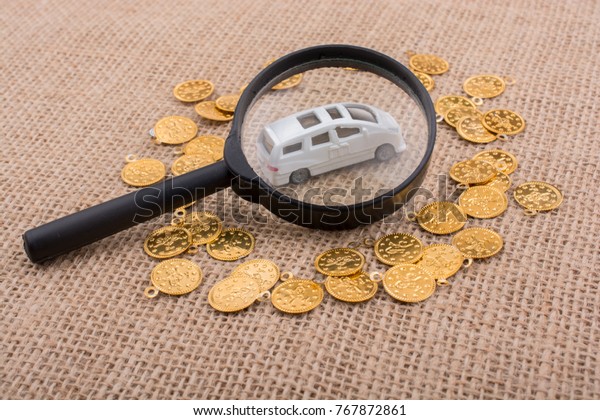 Fake gold\
coins and toy car under magnifying\
glass
