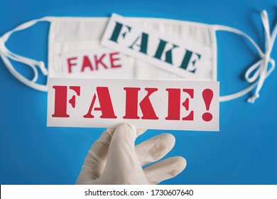 FAKE. Hand In Medical Rubber Gloves Holds An Inscription On A Blue Background With A White Respiratory Mask. Concept Of Coronavirus Fake Hoax Covid-19 Sars-cov-2 Alert For Hoax Fake News.