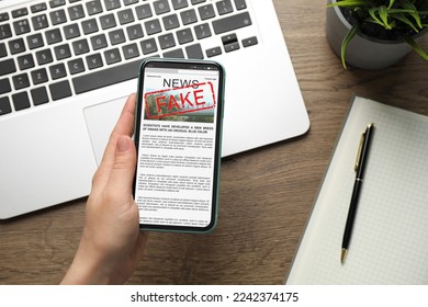 Fake information. Woman using mobile phone to read news at wooden table, closeup. Top view - Shutterstock ID 2242374175