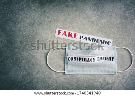 Fake pandemic. Conspiracy theory. Text on a gray vintage background. Vignette. Disposable surgical mask.