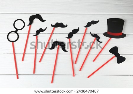Fake paper mustaches, bow tie, hat and monocle party props on white wooden background, flat lay