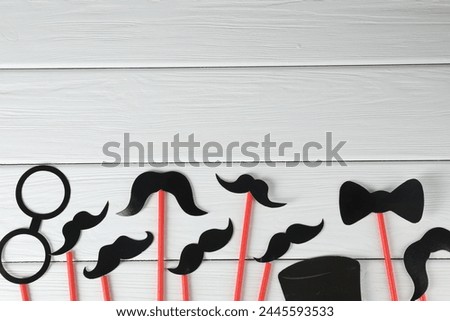 Fake paper mustaches, bow tie and monocle party props on white wooden background, flat lay. Space for text