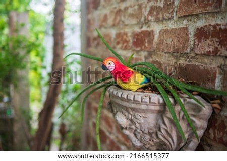 Fake parrot bird  on tree pot attached on brick wall with blur foliage green bokeh.