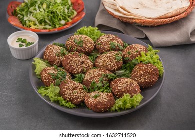 Falafel (Egyptian Ta'ameya) plate, tahini sauce, lettuce salad and Arabic flat bread on grey background 