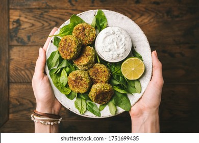 Falafel with yogurt tzatziki dip sauce. Woman's hands holding plate of vegetarian spinach falafel served with greek yogurt tzatziki sauce