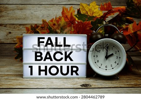 Fall Back 1 Hour text with alarm clock and maple leaf decoration on wooden background