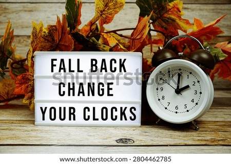 Fall back change your clocks text with alarm clock and maple leaf decoration on wooden background
