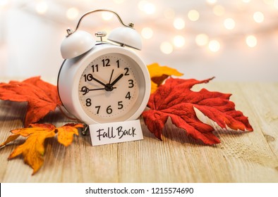 Fall Back Daylight Saving Time concept with white clock and autumn leaves, soft bokeh background on wooden board - Shutterstock ID 1215574690