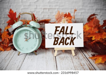 Fall Back text message with alarm clock and maple leaves on wooden background