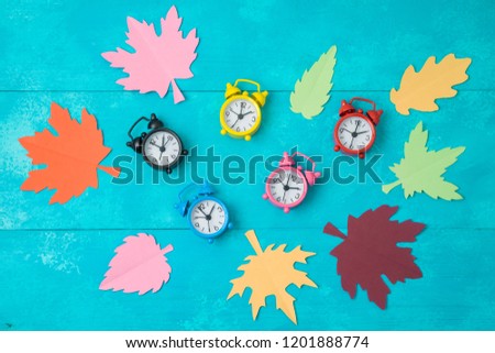 Fall back time change concept. Creative composition with alarm clock and paper autumn leaves. Top view from above