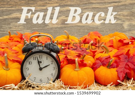 Fall Back time change message with a retro alarm clock with orange pumpkins with fall leaves on straw hay with weathered wood