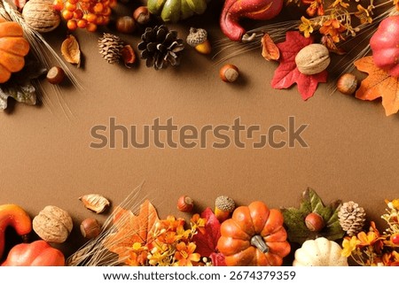 Fall border composition on brown background with pumpkins, pinecones, nuts, wheat stalks, berries and colorful leaves