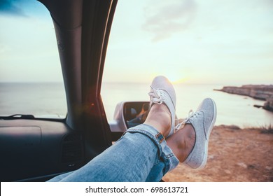 Fall car trip in sunset. Freedom travel concept. Spending weekend in roadtrip. Woman feet on car window, watching the sea.