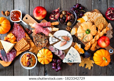 Fall charcuterie table scene against a dark wood background. Assorted cheese and meat appetizers. Top down view.