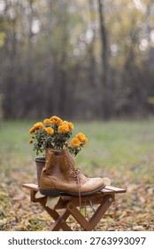Fall composition of brown leather boots with orange chrysanthemum flowers outdoors in a forest