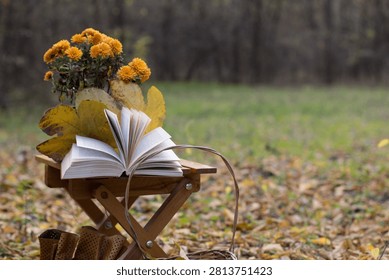 Fall composition of brown leather boots with orange chrysanthemum flowers, and a basket outdoors in a forest