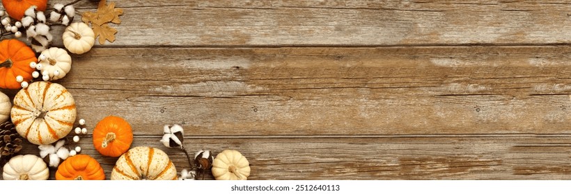 Fall corner border of pumpkins, leaves and natural decor over a rustic wood banner background. Top down view with copy space. White, brown and orange colors.