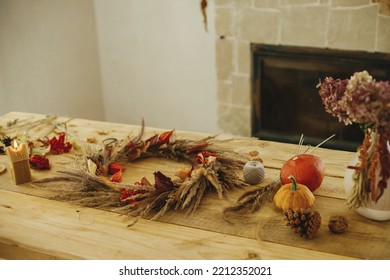 Fall decor and arrangement in farmhouse. Wreath, candle, dried grass, thread, pumpkins and candle on wooden table. Making stylish autumn wreath on rustic table at fireplace