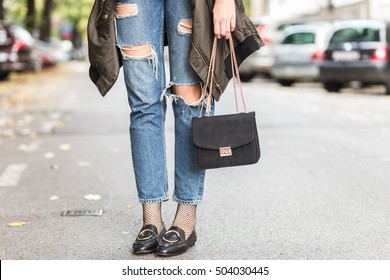 Fall Fashion Outfit Details. Fashionable Woman Wearing Ripped Jeans With Loafers, Oversized Bomber Jacket And A Trendy Black Bag.

