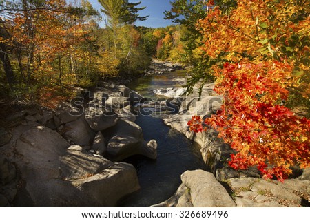 Fall foliage and smooth, sculpted boulders along the Baker River in Warren, New Hampshire on a sunny day in autumn.