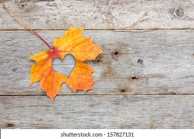 Fall In Love Photo Metaphor. Maple Leaf With Heart Shape On The Wooden Background