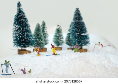 fall of a miniature figure skier in a group. Ski accident while going downhill. white background with fir-trees