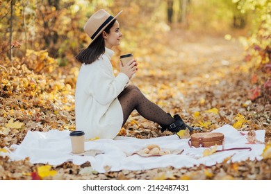 Fall Picnic In The Park. Girl Sitting On Plaid With Coffee In Hand And Enjoying Cozy Picnic. Autumn Picnic In Nature. 