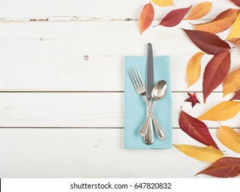 Fall Place Setting With Colorful Leaves, A Teal Cloth Napkin And Silverwarel On Distressed White Shiplap Board Background With Room Or Space For Copy, Text, Or Words.  It's A Flat Lay And Horizontal