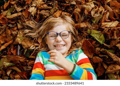 Fall portrait of little preschool girl in autumn park on warm october day with oak and maple leaf. Child with lot of leaves. Family outdoor fun in fall. Kid smiling. Healthy funny child with glasses - Powered by Shutterstock