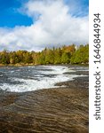 Fall Scene featuring water rapids and cascade with flowing water and rocks on a sunny day in late fall with blue sky and white clouds