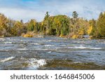 Fall Scene featuring water rapids and cascade with flowing water and rocks on a sunny day in late fall with blue sky and white clouds