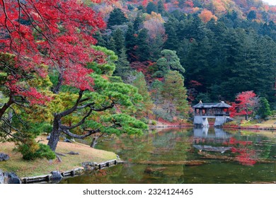 Fall scenery of a beautiful garden in Shugakuin Imperial Villa 修学院離宮 in Kyoto, Japan, with fiery maple foliage in a forest reflected in the peaceful lake water and Chitose Bridge 千歳橋 in background