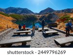 Fall scenery of Mikurigaike Pond (a volcanic crater lake in Murodo Daira of Tateyama Kurobe Alpine Route, Toyama, Japan) with golden grassy meadows on the lakeside and majestic mountains in background