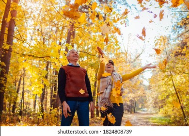 Fall Season. Family Couple Throwing Leaves In Autumn Forest. Senior People Having Fun Outdoors Enjoying Nature