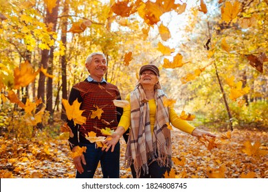 Fall Season. Family Couple Throwing Leaves In Autumn Forest. Senior People Having Fun Outdoors Enjoying Nature