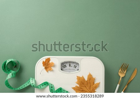 Fall season fitness plan. Top view shot displaying scale, tape measure, fork, knife, maple leaves on green background. Customize with text or promotional material