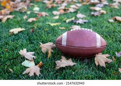 Fall season football background image. The perfect symbols of Autumn, fallen leaves and American Football. The ball sitting on the grass on a crisp fall day	 - Shutterstock ID 2147632943