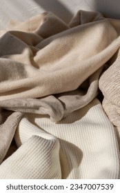 Fall season woman fashion wardrobe concept. Messy crumpled wool and cotton warm neutral beige pastel knitted clothes, knitwear in sunlight with shadow.