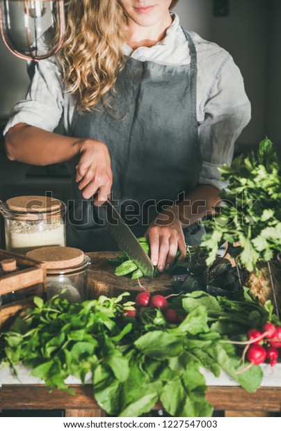 Fall\
seasonal vegetarian, vegan dinner cooking. Woman in linen apron\
cutting green vegetable ingredients on concrete kitchen counter.\
Slow food, comfort food, healthy diet, clean\
eating