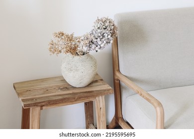 Fall still life photo. Rustic textured vase with dry hydrangea flowers on old wooden bench. Blurred linen mid century sofa background. White wall. Scandinavian interior. Boho elegant home decor. - Shutterstock ID 2195595695