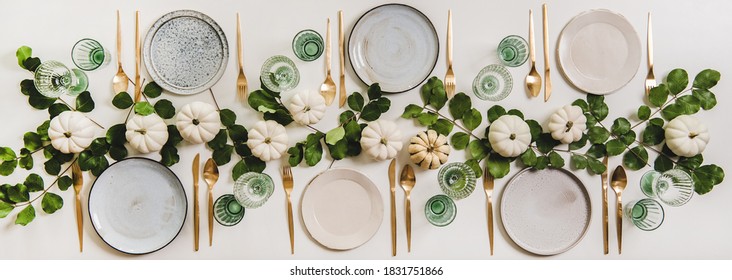 Fall table setting for celebration Thanksgiving or Friendsgiving day, family party or gathering. Flat-lay of plates, cutlery, glassware, pumpkins and leaves over plain white table background, top view