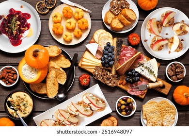 Fall theme appetizer table scene against a dark wood background. Charcuterie board, pumpkin and apple dips, crostini, cheeses and snacks. Top down view. - Powered by Shutterstock