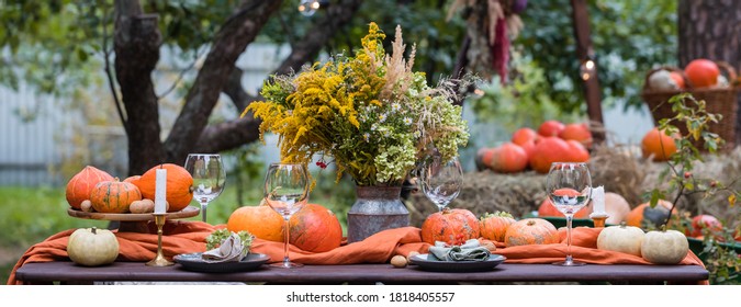 Fall themed holiday table setting arrangement for a seasonal party, glasses, pumpkins, candles, field flowers - Powered by Shutterstock