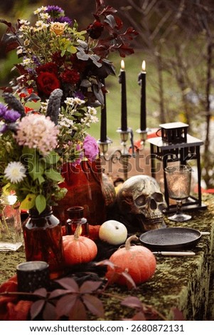 Fall themed holiday table setting arrangement for a seasonal party, glasses, pumpkins, candles, field flowers. Halloween table in the garden with scull, black candles vertical photo