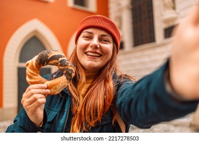 Fall Tourist Woman In A Bright Hat And Autumn Jacket Holding Baked Obwarzanek Traditional Polish Cuisine Snack Bagel On Old City Market Square In Krakow 