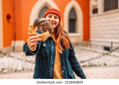 Fall Tourist Woman In A Bright Hat And Autumn Jacket Holding Baked Obwarzanek Traditional Polish Cuisine Snack Bagel On Old City Market Square In Krakow 